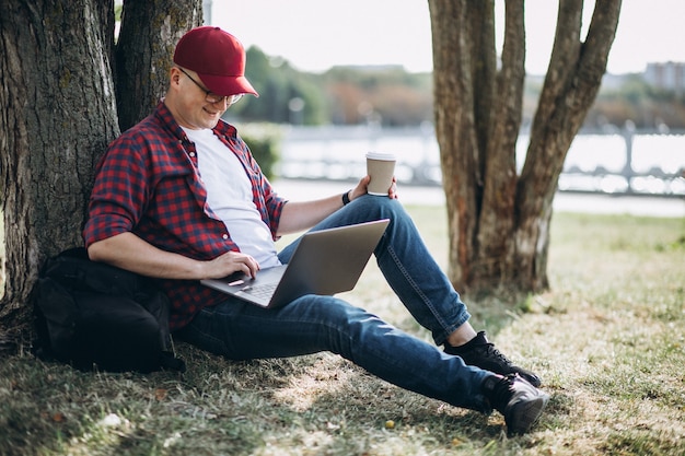 Junger männlicher Student, der an einem Computer im Park arbeitet