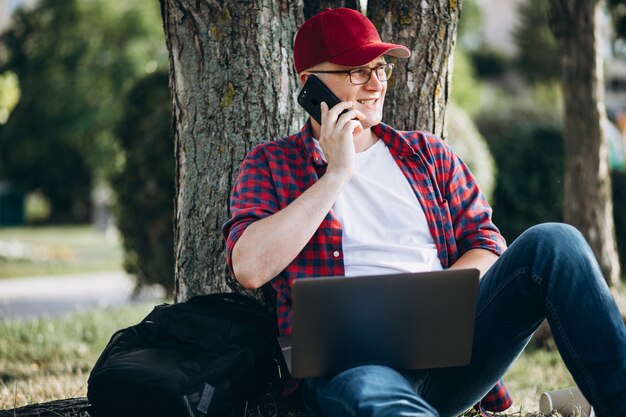 Junger männlicher Student, der an einem Computer im Park arbeitet