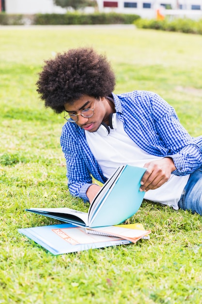 Kostenloses Foto junger männlicher student, der auf dem rasen das buch lesend sich lehnt