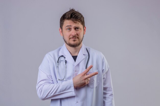 Junger Mann Arzt trägt weißen Kittel und Stethoskop zeigt Nummer zwei mit Fingern oder Siegeszeichen