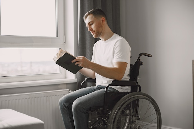 Junger Mann behindert. Mann, der ein Buch im Rollstuhl liest und zu Hause bleibt.