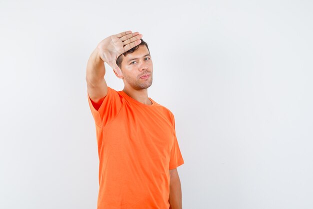 Junger Mann, der ablehnende Geste im orangefarbenen T-Shirt zeigt und müde aussieht