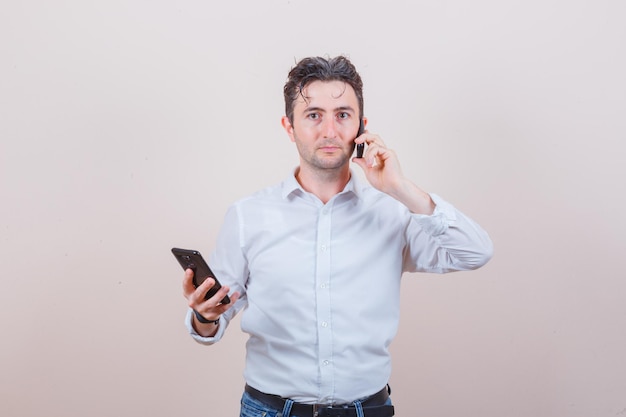 Junger Mann, der am Handy spricht, Smartphone in Hemd, Jeans hält