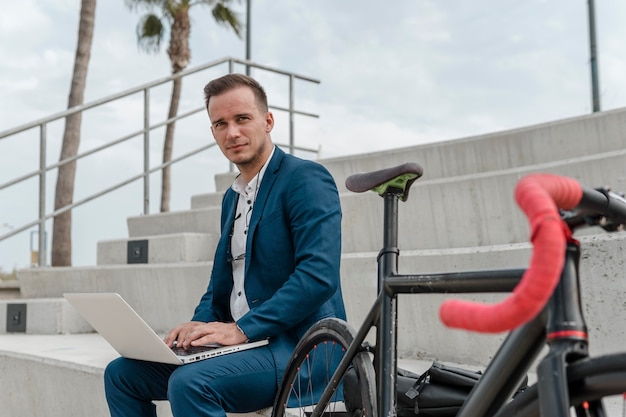 Junger Mann, der am Laptop neben seinem Fahrrad arbeitet