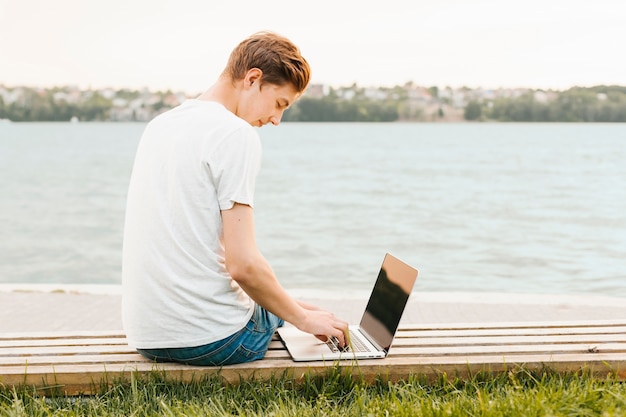 Junger Mann, der an dem Laptop durch den See arbeitet