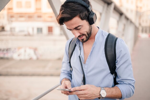 Junger Mann, der auf Brücke unter Verwendung des Smartphone steht