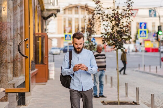 Junger Mann, der auf Bürgersteig unter Verwendung des Mobiltelefons steht