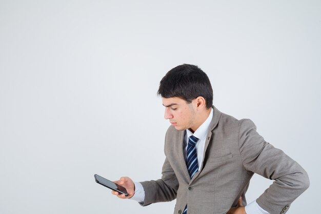 Junger Mann, der auf das Telefon schaut und die Hand im Anzug auf der Hüfte hält