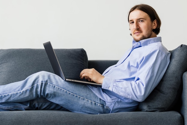Junger Mann, der auf der Couch am Laptop arbeitet