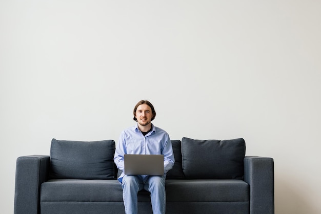 Junger Mann, der auf der Couch am Laptop arbeitet