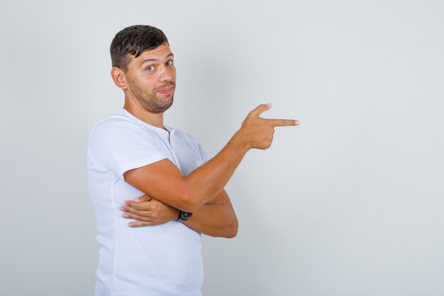 Junger Mann, der auf etwas mit Finger im weißen T-Shirt zeigt und positiv schaut. .