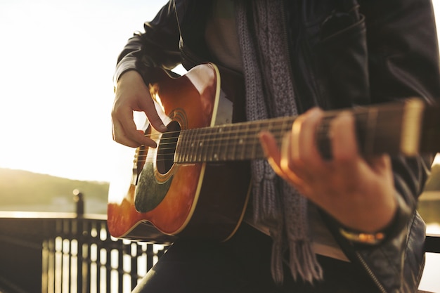 Junger Mann, der auf Gitarre am See spielt