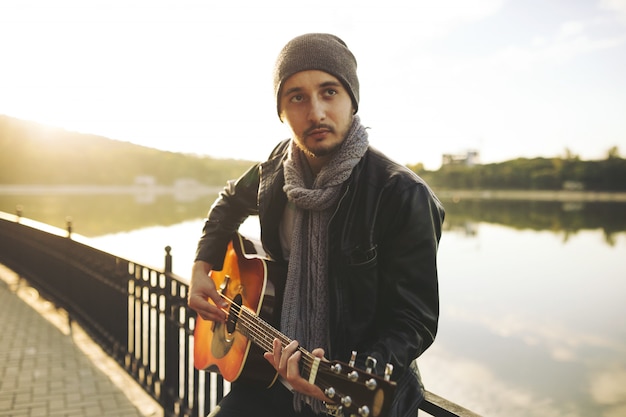 Junger Mann, der auf Gitarre am See spielt