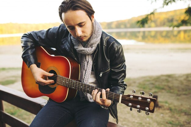 Junger Mann, der auf Gitarre am See spielt