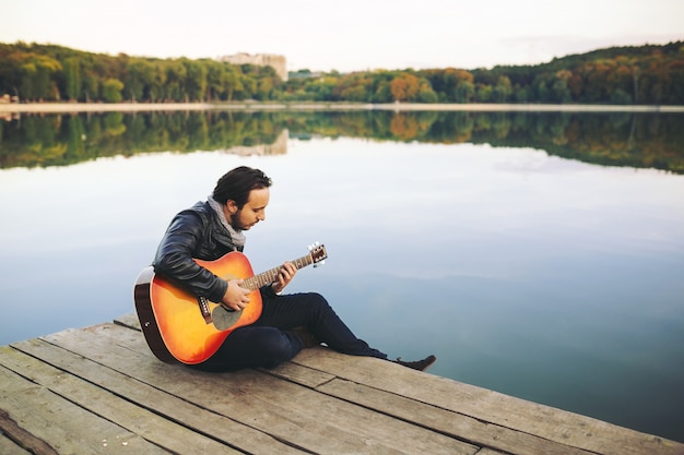 Junger Mann, der auf Gitarre am See spielt