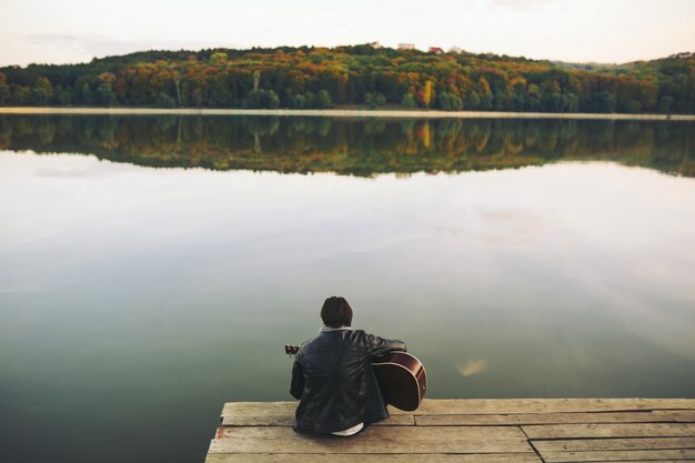 Junger Mann, der auf Gitarre am See spielt