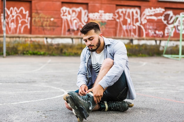 Junger Mann, der auf rollerskate am Gericht im Freien sich setzt