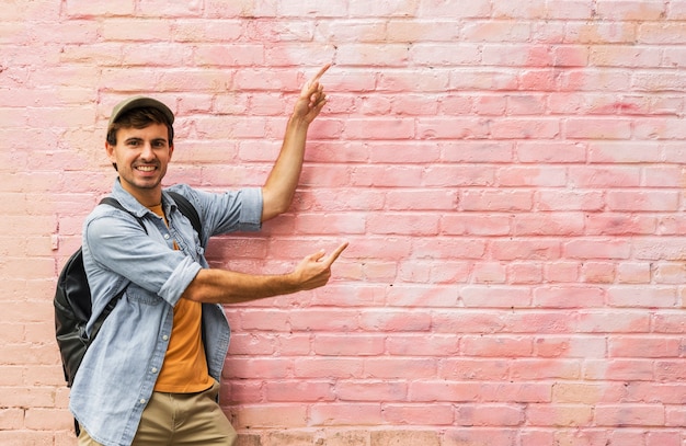 Junger Mann, der auf rosa Wand zeigt