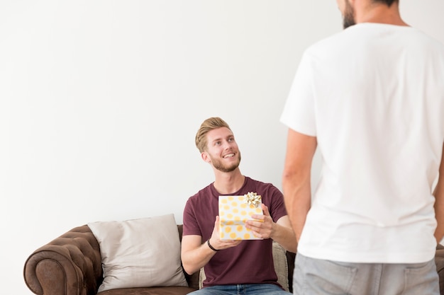 Kostenloses Foto junger mann, der auf sofa mit der geschenkbox betrachtet seinen freund sitzt