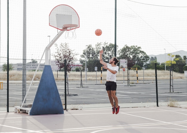 Junger Mann, der Basketball im Band springt und wirft