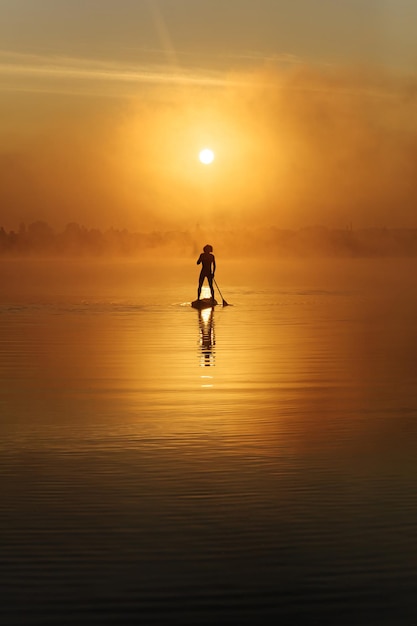 Junger Mann, der bei erstaunlichem Sonnenaufgang im Sup-Surfen übt