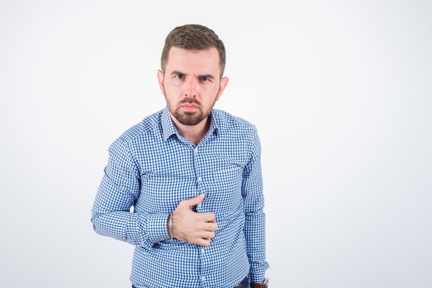 Junger mann, der beim betrachten der kamera im hemd aufwirft und ernsthafte vorderansicht schaut.