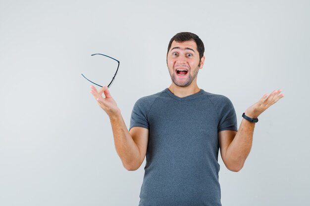 Junger Mann, der Brille im grauen T-Shirt hält und fröhlich schaut