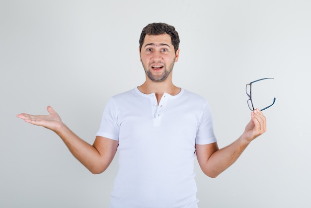 Junger Mann, der Brille mit offenen Armen im weißen T-Shirt hält und glücklich schaut