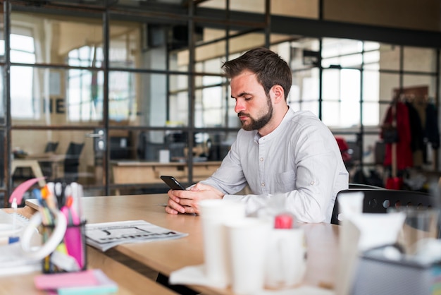 Junger Mann, der den Smartphone sitzt im Büro verwendet