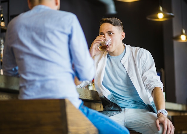 Kostenloses Foto junger mann, der den whisky mit seinem freund am restaurant genießt