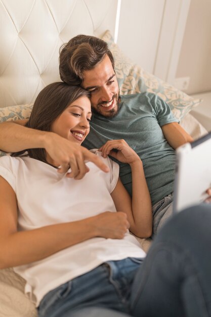 Junger Mann, der der Freundin Tablette auf Bett zeigt