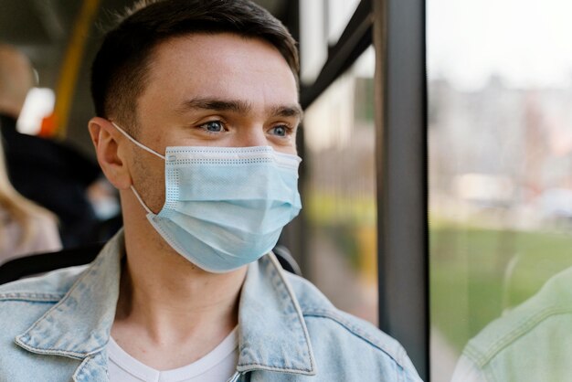 Junger Mann, der durch Stadtbus reist, der chirurgische Maske trägt