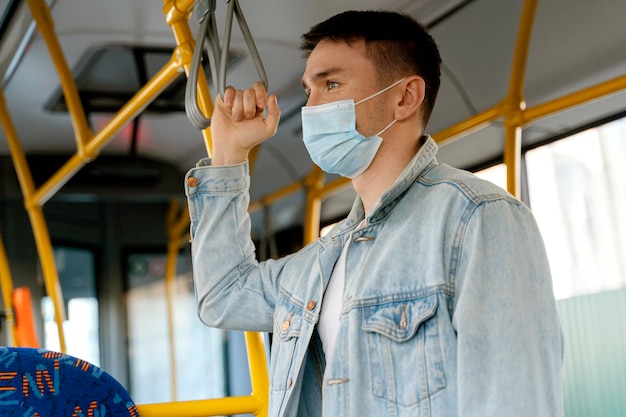 Junger Mann, der durch Stadtbus reist, der chirurgische Maske trägt