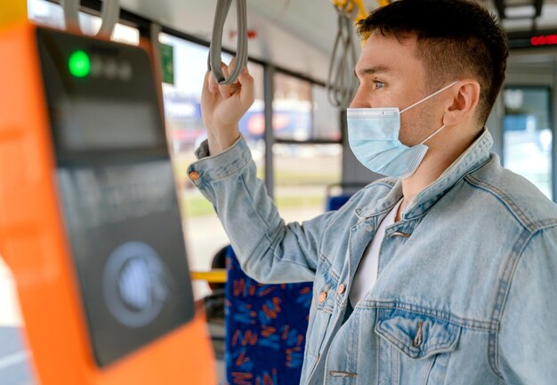 Junger Mann, der durch Stadtbus reist, der chirurgische Maske trägt