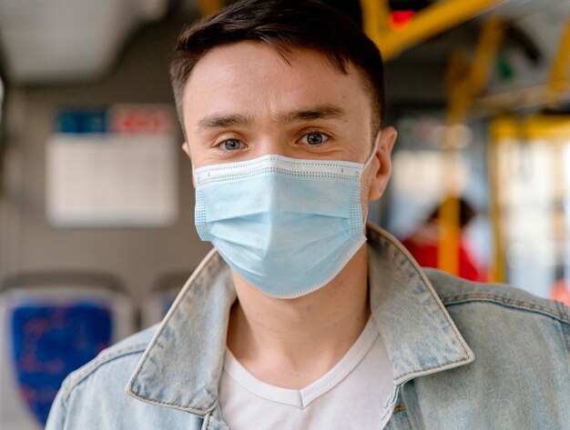 Junger Mann, der durch Stadtbus reist, der chirurgische Maske trägt