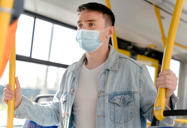 Junger Mann, der durch Stadtbus reist, der chirurgische Maske trägt