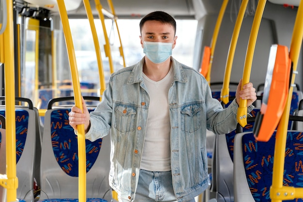 Junger Mann, der durch Stadtbus reist, der chirurgische Maske trägt