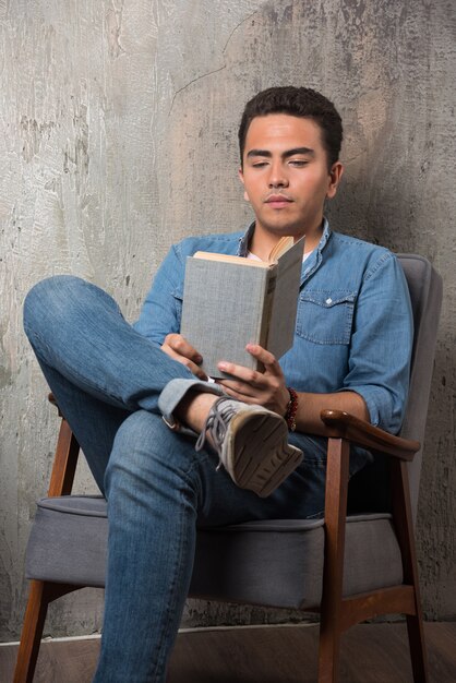 Junger Mann, der ein Buch liest und auf Stuhl sitzt. Hochwertiges Foto