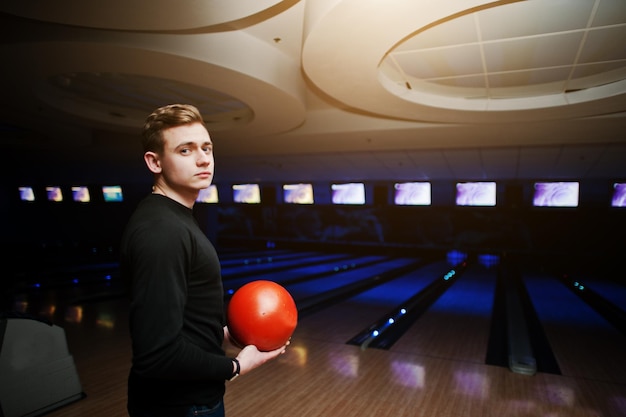 Junger Mann, der eine Bowlingkugel hält, die mit ultraviolettem Licht gegen Bowlingbahnen steht