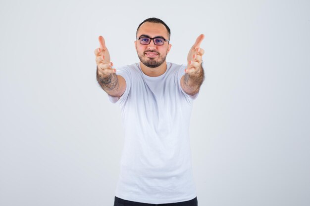 Junger Mann, der eine Brille trägt und sich die Hände ausstreckt, als er etwas in weißem T-Shirt und schwarzer Hose erhält und glücklich aussieht?