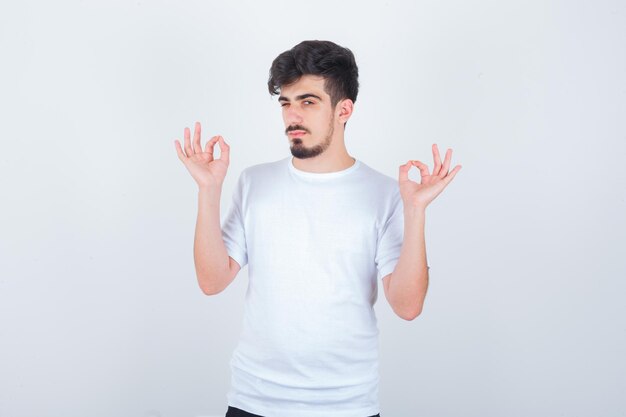 Junger Mann, der eine gute Geste im T-Shirt zeigt und glücklich aussieht