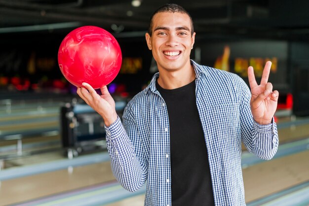 Junger Mann, der eine rote Bowlingkugel hält