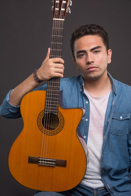 Junger Mann, der eine schöne Gitarre auf schwarzem Hintergrund hält. Hochwertiges Foto