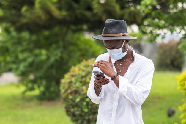 Junger Mann, der eine schützende Gesichtsmaske mit seinem Telefon im Freien trägt