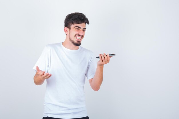 Junger Mann, der eine Sprachnachricht auf dem Handy im T-Shirt aufnimmt und glücklich aussieht