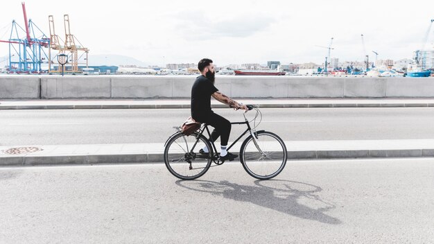 Junger Mann, der Fahrrad auf Straße nahe dem Hafen fährt