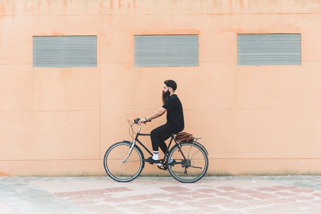 Junger Mann, der Fahrrad vor beige Wand fährt