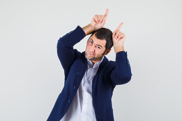 Junger Mann, der Finger über Kopf als Stierhörner im Hemd hält