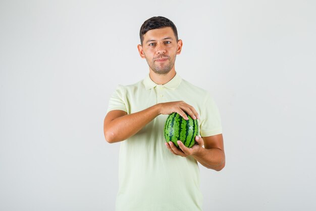 Junger Mann, der frische Wassermelone im T-Shirt hält und froh schaut.