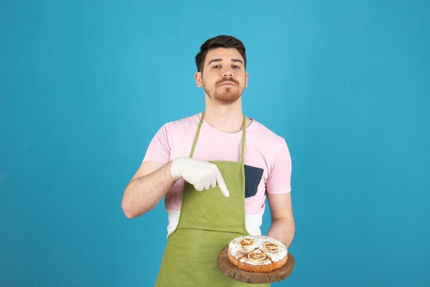 Junger Mann, der frischen Kuchen hält und mit dem Finger darauf zeigt.